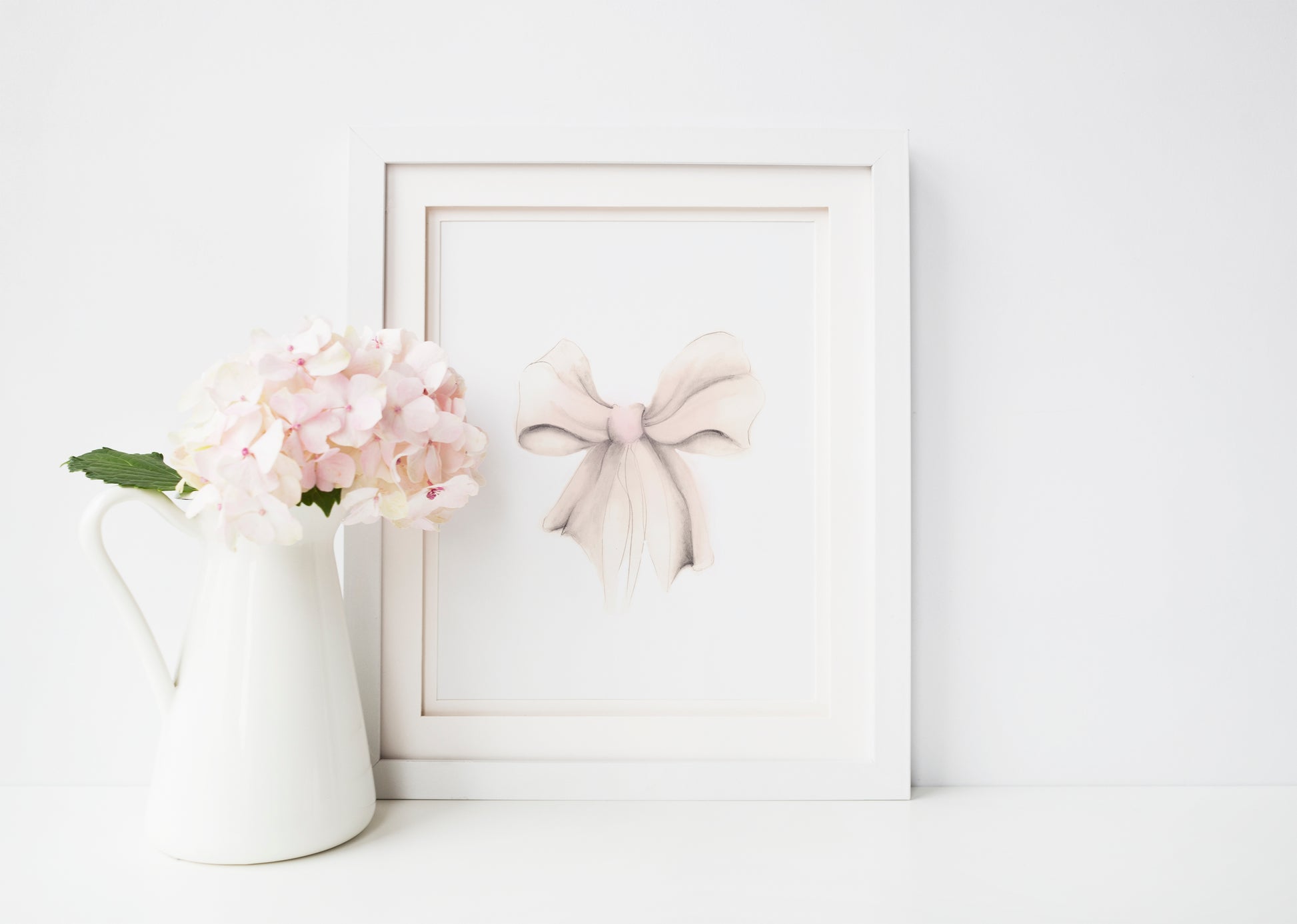 Sketch of a bow in tones of pink and sepia beige. The bow is on a plain white background and is framed in a wood frame that sits on a wood floor - Studio Q - Art by Nicky Quartermaine Scott
