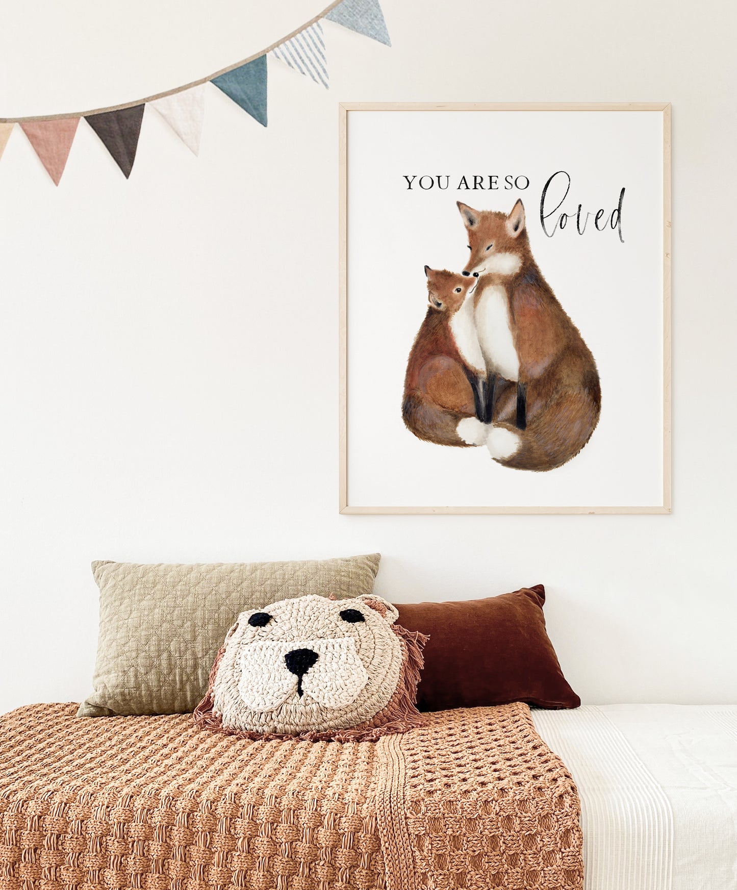 Artwork painting of a mother and baby fox with the words You are So Loved. The artwork is on a plain white background and is framed in a light wood frame. The picture hangs on a light colored wall over a child's bed.  Art by Studio Q - Art by Nicky Quartermaine Scott