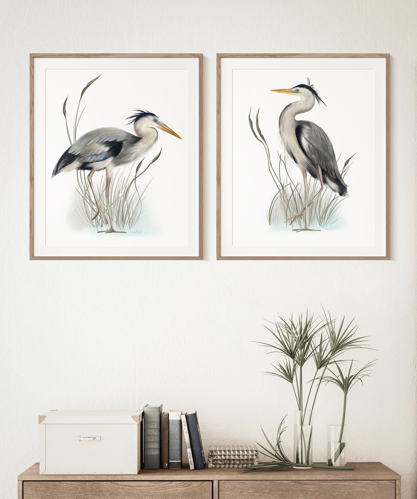 Set of 2 Great Blue Heron Birds in tall grasses art illustration prints on white backgrounds in wood frames hung on a white wall. The frames sit above a credenza in a living room - Studio Q - Art by Nicky Quartermaine Scott