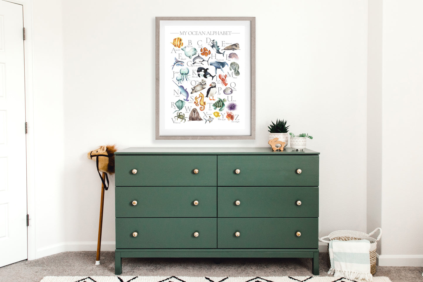 Colorful ocean animal alphabet print for kids with underwater animals from A thru Z framed in a light wood frame hanging on a wall above a green dresser in a kids bedroom- Studio Q - Art by Nicky Quartermaine Scott